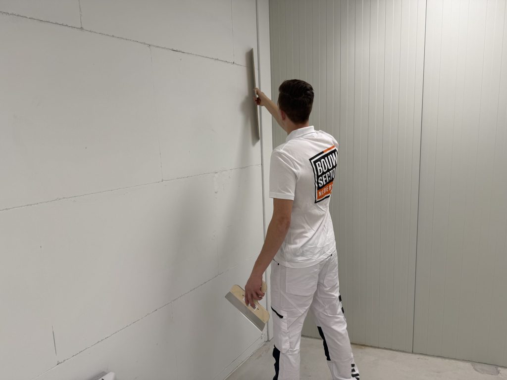 Stukadoor werkt een lange wand van gipsplaat af en haalt de spaan langs de hoek richting plafond