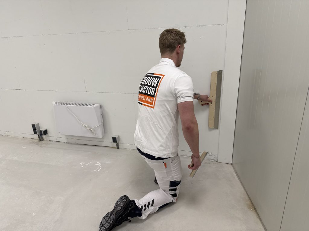 Stukadoor op een knie werkt de onderkant van een wand bij met een lange spaan
