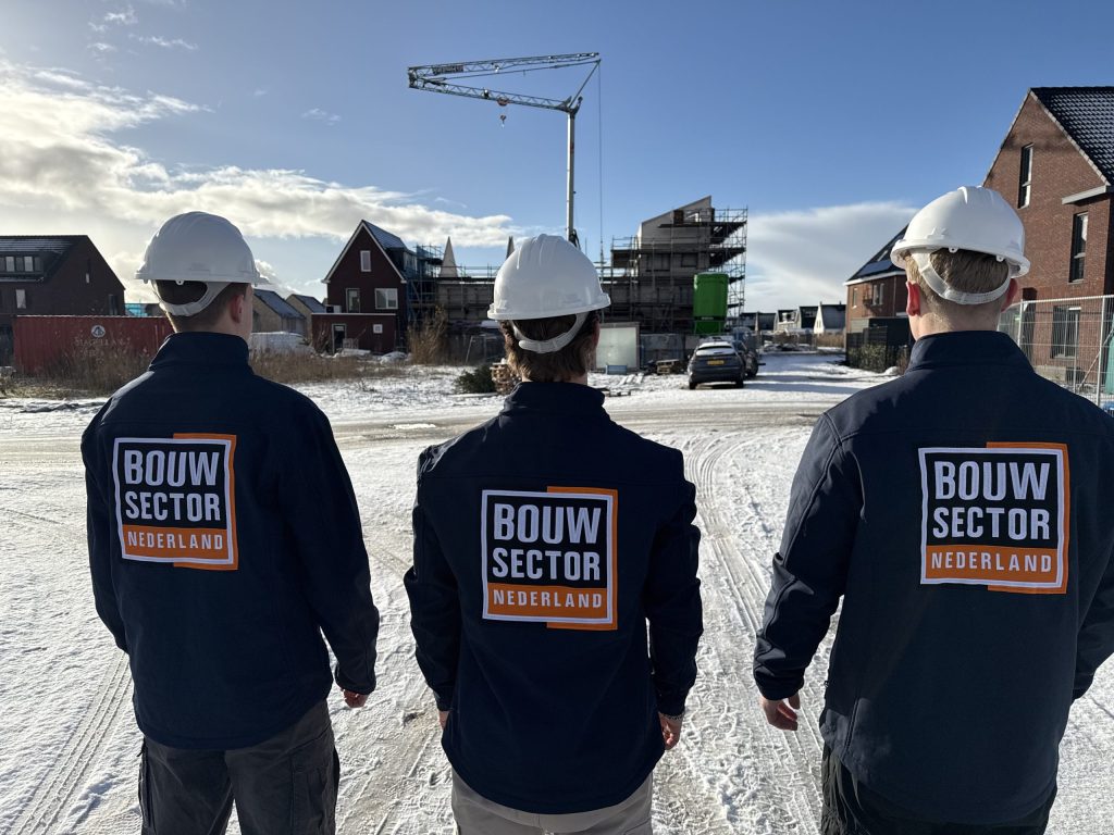 Drie medewerkers van Bouwsector Nederland met bouwhelm op een besneeuwde weg tussen nieuwe bakstenen woningen