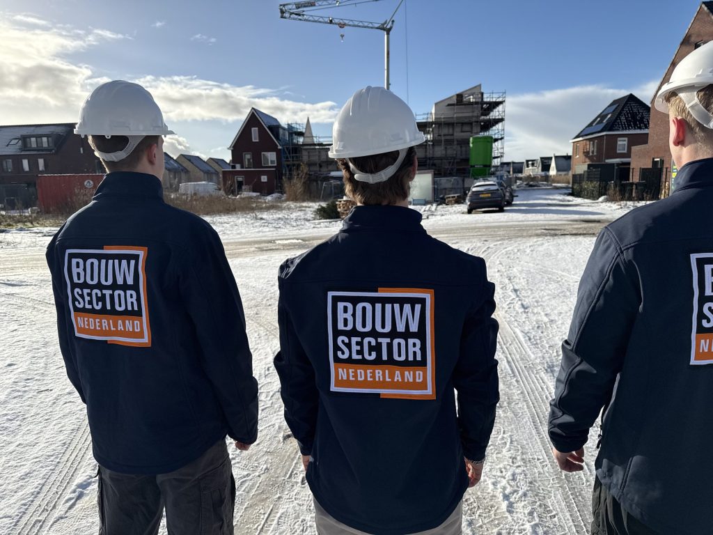 Medewerkers van Bouwsector Nederland met witte helm kijken uit over een nieuwbouwwijk in aanbouw